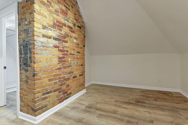 bonus room featuring brick wall, light hardwood / wood-style floors, and vaulted ceiling