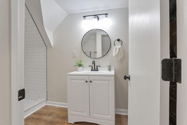 bathroom featuring hardwood / wood-style floors, vanity, lofted ceiling, and tiled shower