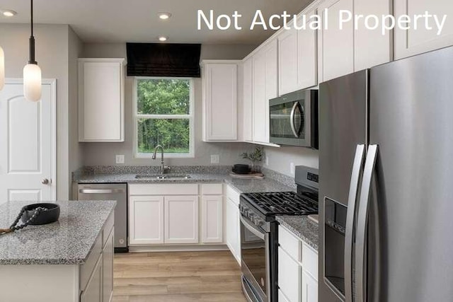 kitchen with stainless steel appliances, white cabinetry, light stone countertops, and sink