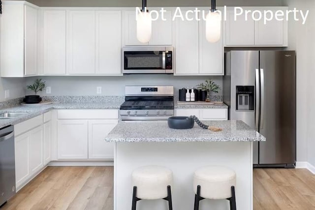 kitchen featuring hanging light fixtures, light stone countertops, appliances with stainless steel finishes, and white cabinets