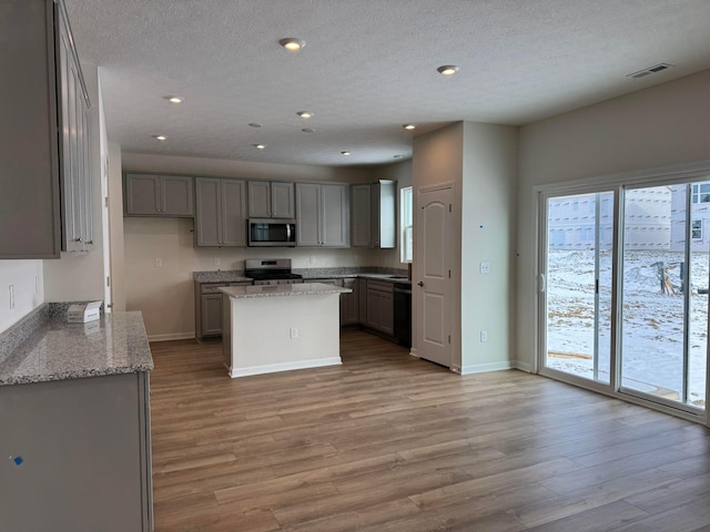 kitchen with gray cabinetry, a center island, light wood-type flooring, stainless steel appliances, and light stone countertops