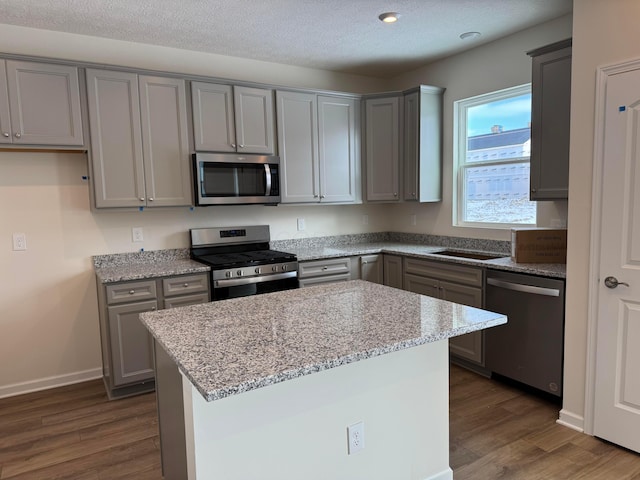 kitchen featuring stainless steel appliances, light stone countertops, gray cabinetry, and dark hardwood / wood-style flooring