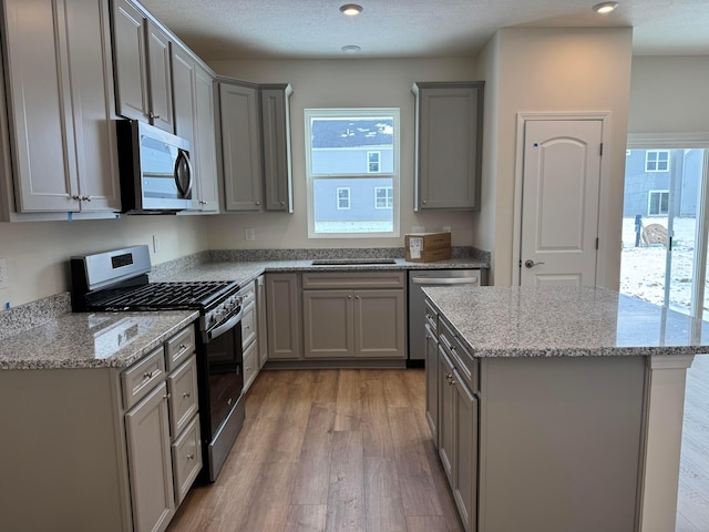 kitchen featuring gray cabinetry, light stone countertops, hardwood / wood-style flooring, and stainless steel appliances