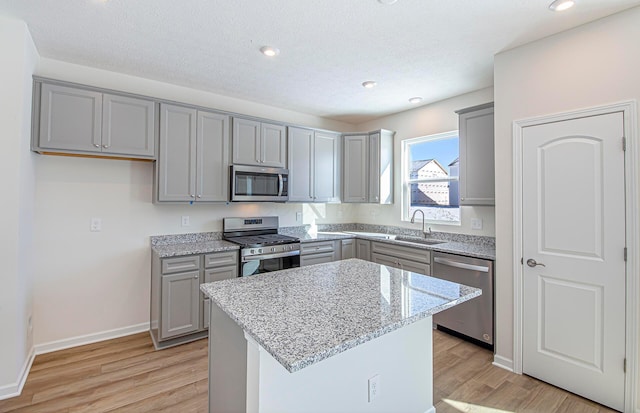 kitchen with stainless steel appliances, a center island, sink, gray cabinets, and light stone counters