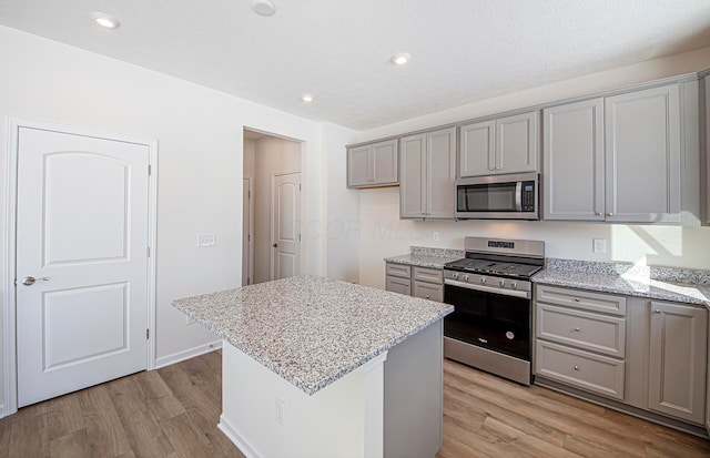 kitchen featuring light hardwood / wood-style flooring, light stone counters, a kitchen island, gray cabinetry, and stainless steel appliances