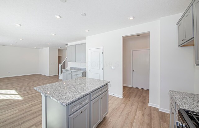 kitchen featuring stainless steel range oven, gray cabinetry, light stone counters, light hardwood / wood-style floors, and a kitchen island