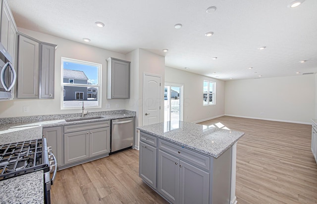 kitchen featuring sink, light wood-type flooring, a kitchen island, gray cabinetry, and stainless steel appliances