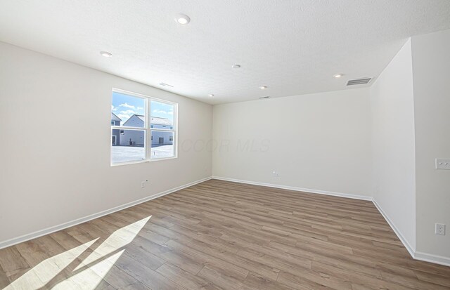 unfurnished room with light wood-type flooring and a textured ceiling