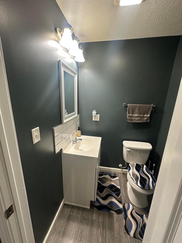 bathroom featuring tasteful backsplash, hardwood / wood-style floors, a textured ceiling, toilet, and vanity