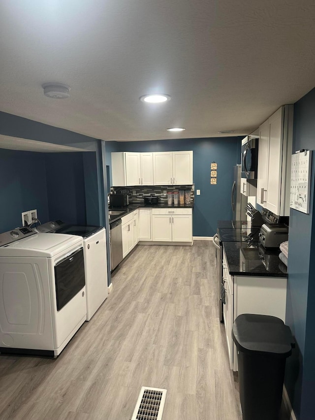 kitchen with backsplash, white cabinets, light hardwood / wood-style floors, stainless steel appliances, and washing machine and clothes dryer