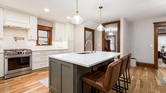 kitchen with white cabinets, a center island with sink, high end range, and sink