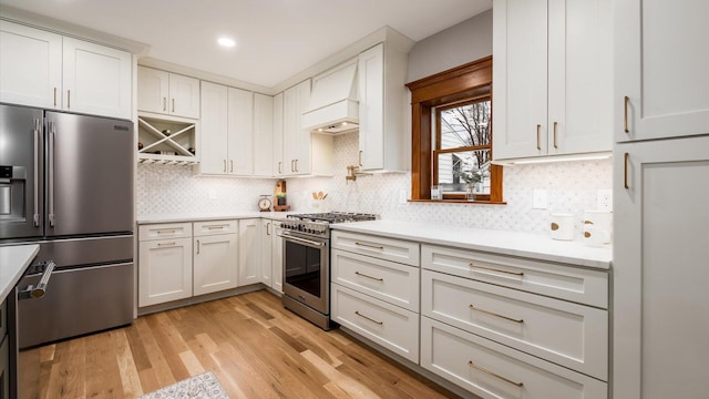 kitchen with premium range hood, white cabinetry, light hardwood / wood-style flooring, and premium appliances