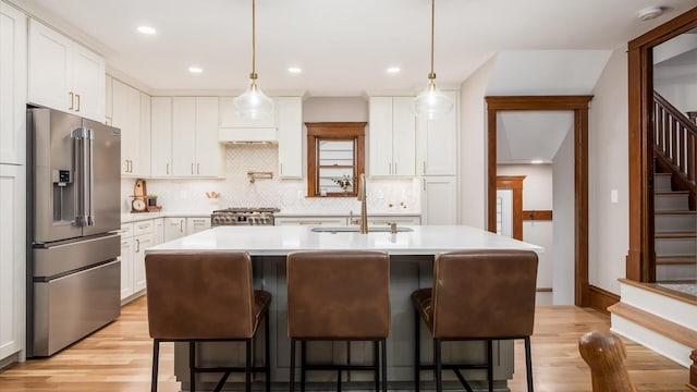 kitchen with appliances with stainless steel finishes, light wood-type flooring, white cabinetry, and an island with sink