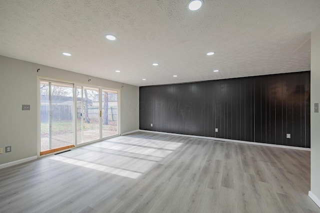 unfurnished room with a textured ceiling, light wood-type flooring, and wooden walls