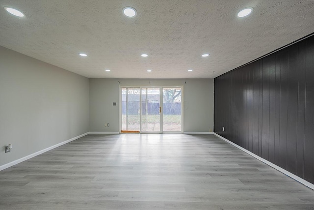 unfurnished room featuring wood walls, light hardwood / wood-style floors, and a textured ceiling