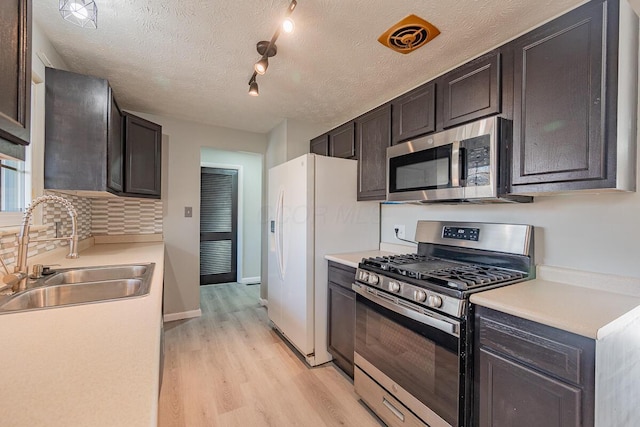 kitchen with appliances with stainless steel finishes, light wood-type flooring, dark brown cabinets, and sink