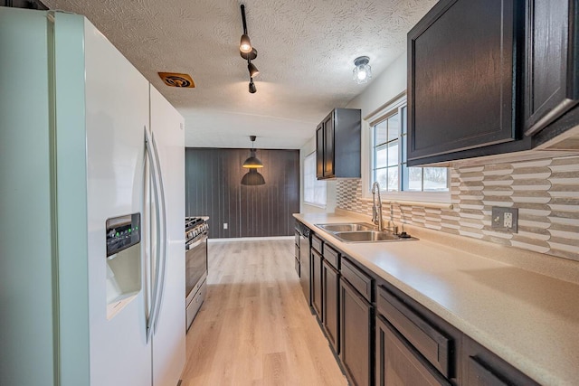 kitchen with white refrigerator with ice dispenser, sink, hanging light fixtures, stainless steel gas range, and a textured ceiling