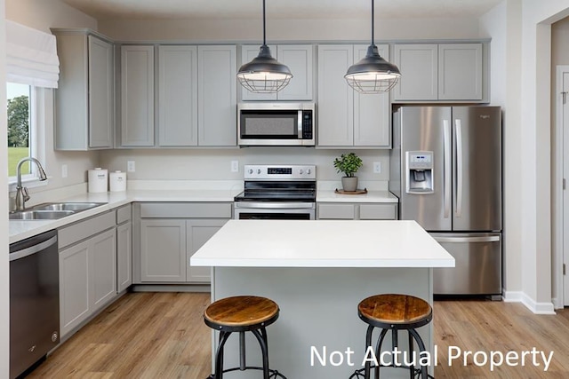 kitchen with a breakfast bar, stainless steel appliances, gray cabinets, light wood-style floors, and a sink