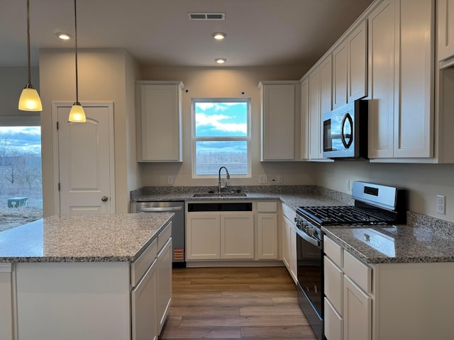 kitchen with light stone counters, a sink, visible vents, light wood-style floors, and appliances with stainless steel finishes