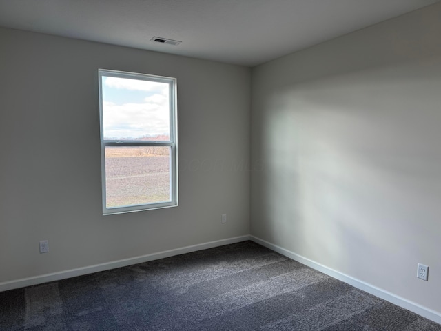 empty room with dark carpet, visible vents, and baseboards