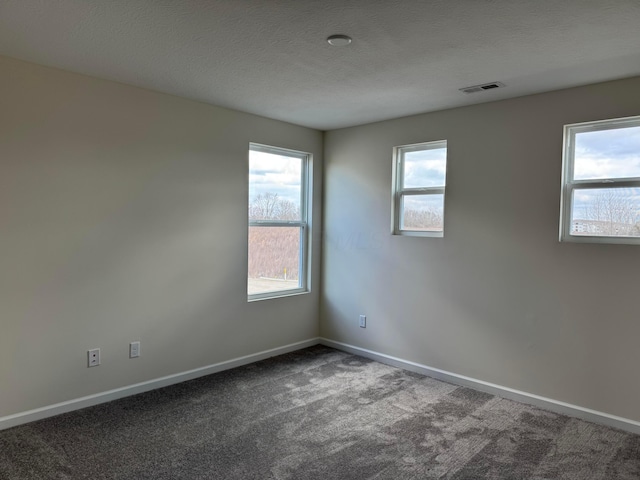 empty room with carpet floors, visible vents, a textured ceiling, and baseboards