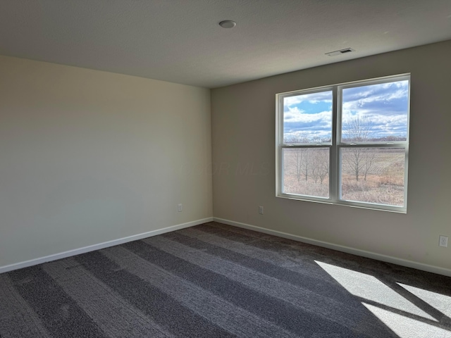 empty room with dark colored carpet, visible vents, and baseboards