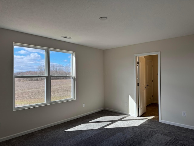 spare room featuring dark colored carpet, visible vents, a textured ceiling, and baseboards