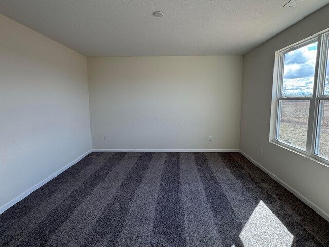 spare room featuring dark carpet, a wealth of natural light, and baseboards