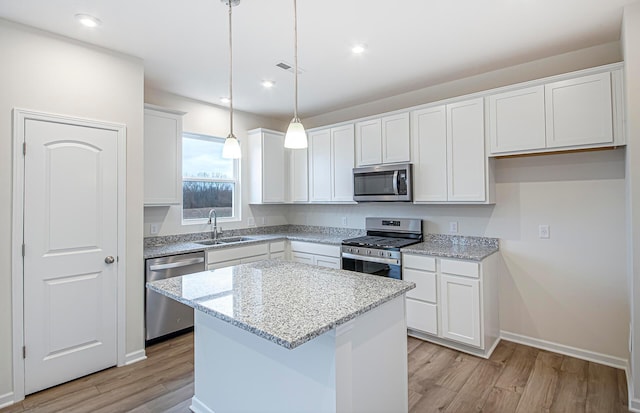 kitchen featuring visible vents, appliances with stainless steel finishes, white cabinets, a sink, and a kitchen island