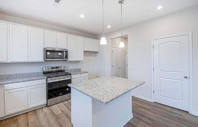 kitchen featuring hanging light fixtures, appliances with stainless steel finishes, white cabinets, a kitchen island, and light wood-type flooring