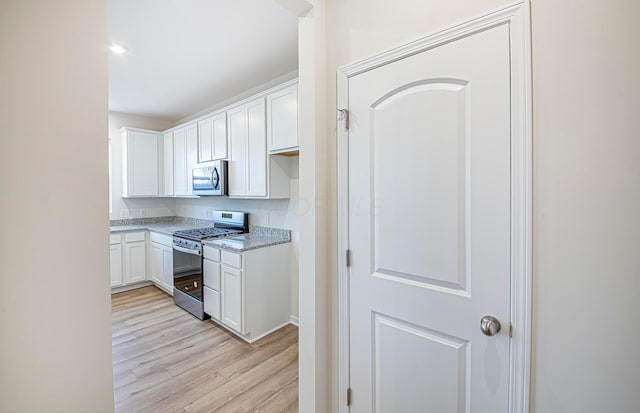 kitchen featuring white cabinets, light wood-style floors, stainless steel appliances, and light stone countertops