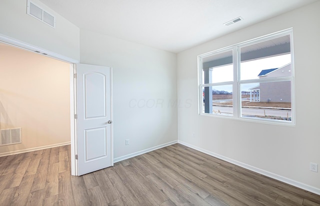 unfurnished room featuring baseboards, visible vents, and wood finished floors