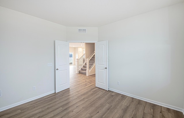 empty room featuring visible vents, stairway, baseboards, and wood finished floors