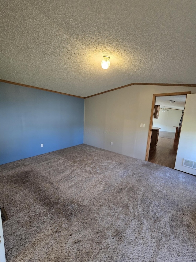 spare room with a textured ceiling, dark carpet, lofted ceiling, and crown molding