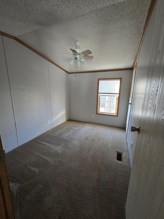 carpeted empty room featuring ceiling fan, crown molding, and a textured ceiling