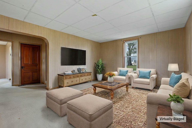 carpeted living room with a drop ceiling and wooden walls