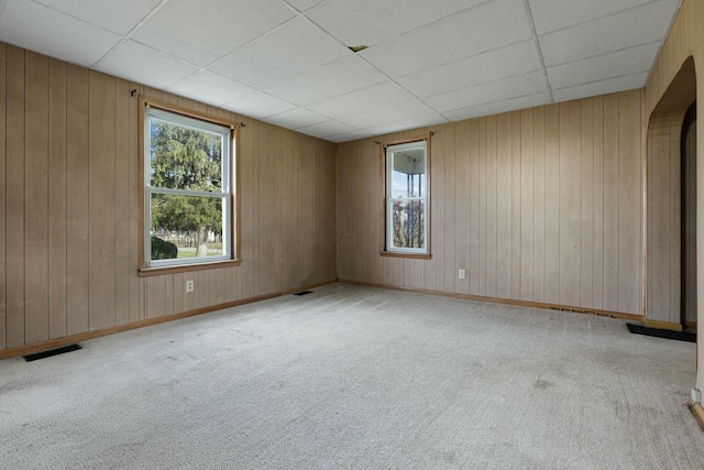 unfurnished room with a paneled ceiling, wood walls, and light colored carpet