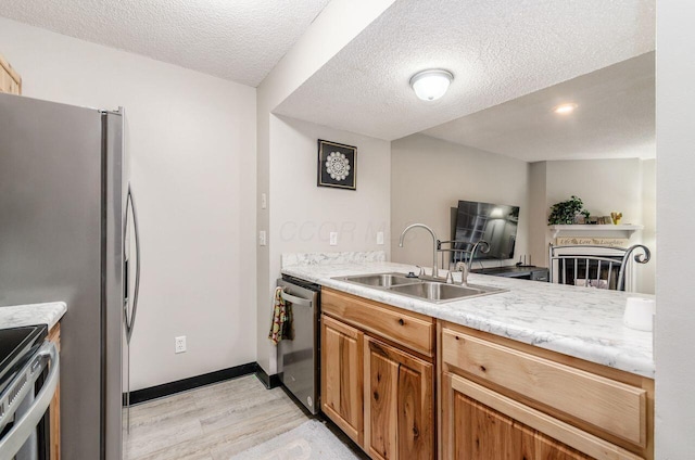 kitchen featuring sink, light hardwood / wood-style floors, a textured ceiling, and appliances with stainless steel finishes