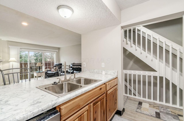 kitchen featuring dishwasher, sink, a textured ceiling, and light wood-type flooring