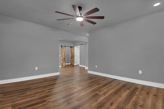 unfurnished room featuring dark hardwood / wood-style floors, ceiling fan, and a barn door