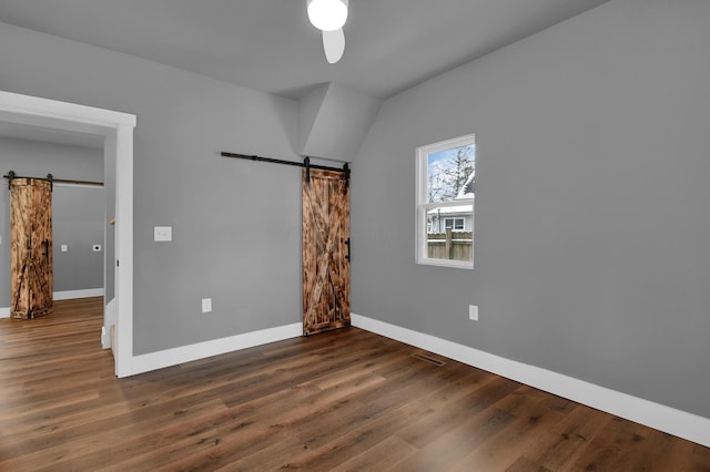 unfurnished room with ceiling fan, a barn door, and dark hardwood / wood-style flooring