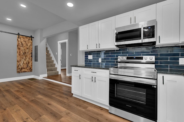 kitchen with tasteful backsplash, white cabinetry, dark stone countertops, stainless steel appliances, and a barn door