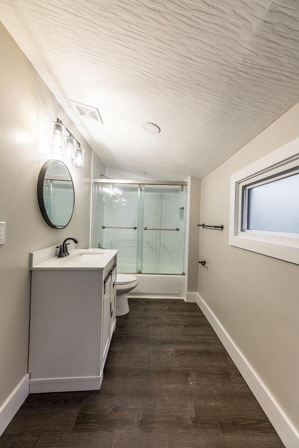 full bathroom featuring vanity, wood-type flooring, enclosed tub / shower combo, toilet, and lofted ceiling