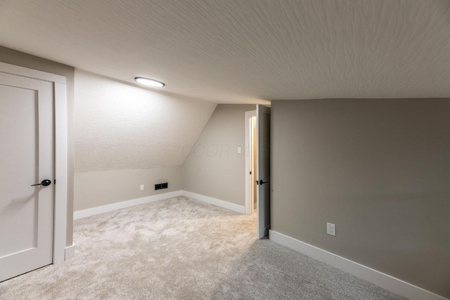 interior space with a textured ceiling, light colored carpet, and vaulted ceiling