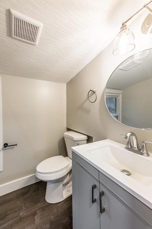 bathroom featuring vanity, wood-type flooring, lofted ceiling, and toilet