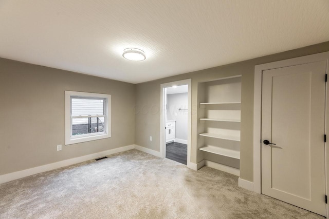 unfurnished bedroom with a textured ceiling, ensuite bathroom, and light carpet