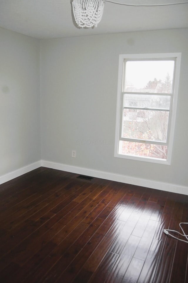 spare room with dark wood-type flooring and an inviting chandelier