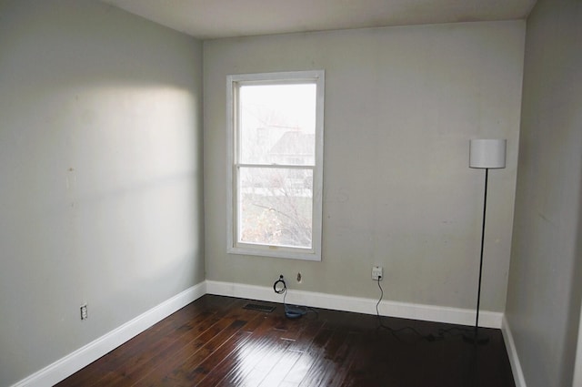 empty room with a wealth of natural light and dark hardwood / wood-style flooring