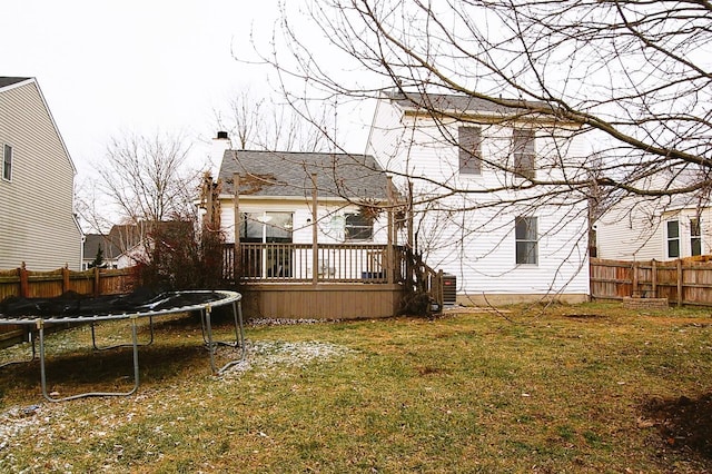 rear view of property featuring a lawn, a wooden deck, and a trampoline