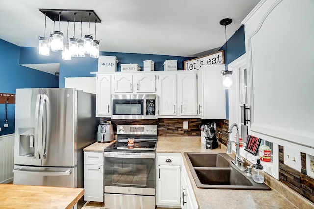 kitchen featuring appliances with stainless steel finishes, vaulted ceiling, sink, pendant lighting, and white cabinetry